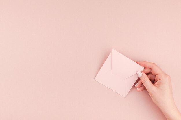 Foto mão cortada de mulher segurando envelope contra fundo rosa