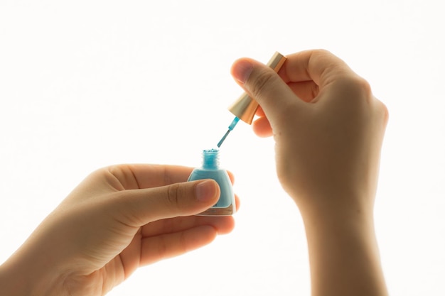 Mão cortada de mulher segurando esmalte de unhas contra fundo branco