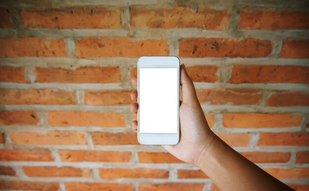 Foto mão cortada de mulher segurando telefone móvel contra uma parede de tijolos