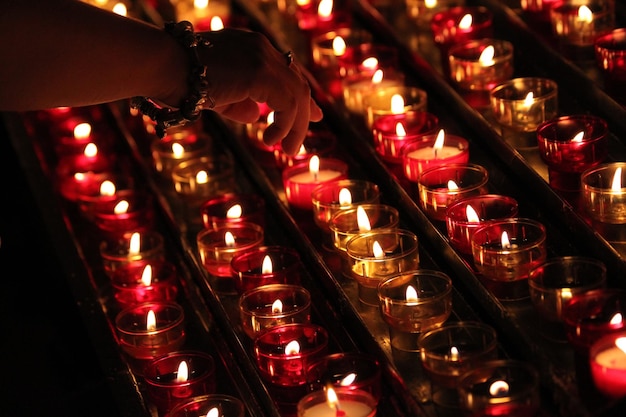 Mão cortada de mulher sobre chá acende velas na sala escura