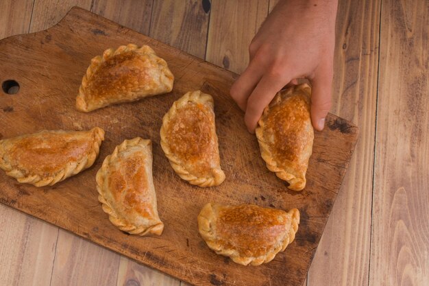 Foto mão cortada de pessoa agarrando comida na tábua de corte empanadas argentinas