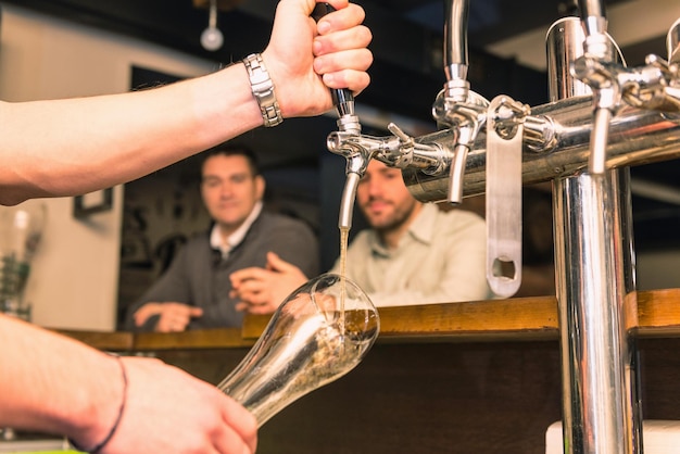 Foto mão cortada de pessoa dispensando cerveja em copo da máquina com homens ao fundo