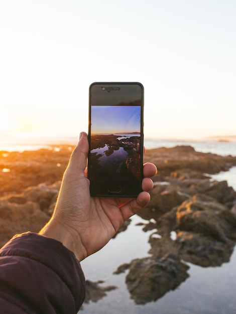 Foto mão cortada de pessoa fotografando em smartphone contra o céu