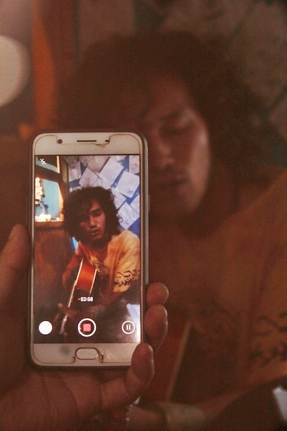 Mão cortada de pessoa fotografando homem tocando guitarra