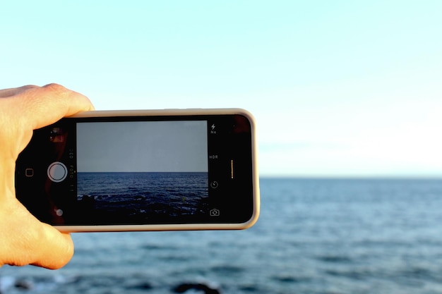 Foto mão cortada de pessoa fotografando o mar contra o céu
