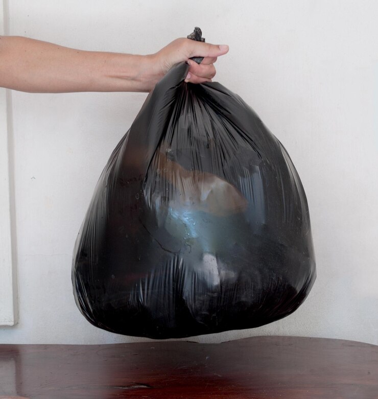 Foto mão cortada de pessoa segurando saco de lixo contra a parede branca
