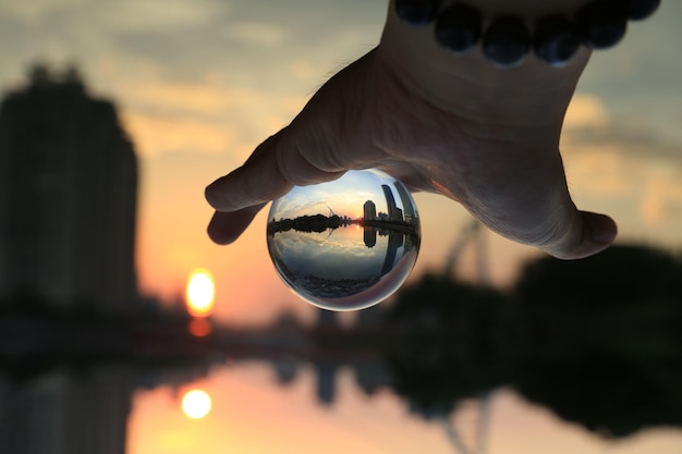 Foto mão cortada de pessoa segurando uma bola de cristal contra o céu durante o pôr do sol