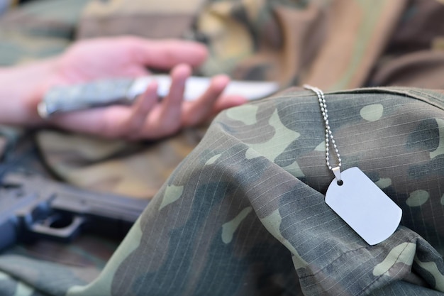 Foto mão cortada de pessoa segurando uma faca sobre roupas de camuflagem