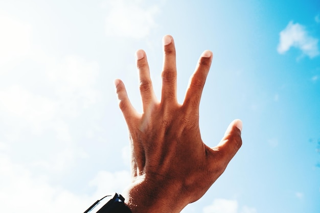 Mão cortada de um homem a fazer gestos contra o céu azul.