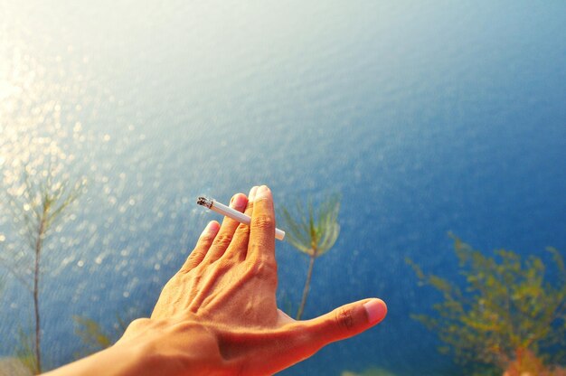 Foto mão cortada de um homem segurando um cigarro sobre o mar