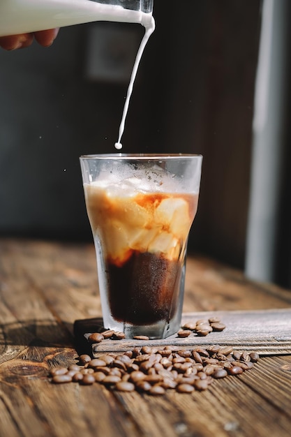 Mão cortada derramando leite em café gelado em uma mesa de madeira