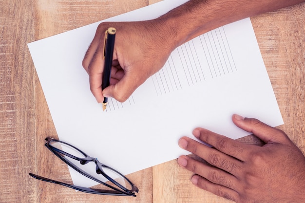 Mão cortada do empresário escrevendo no papel na mesa no escritório