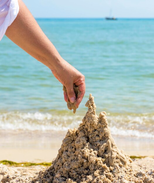 Foto mão cortada fazendo castelo de areia na praia