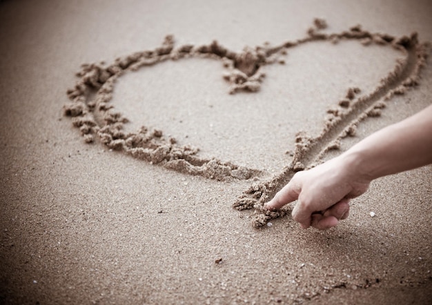 Foto mão cortada fazendo forma de coração na areia na praia