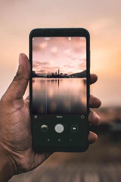 Foto mão cortada fotografando o lago a partir de um telefone móvel durante o pôr do sol