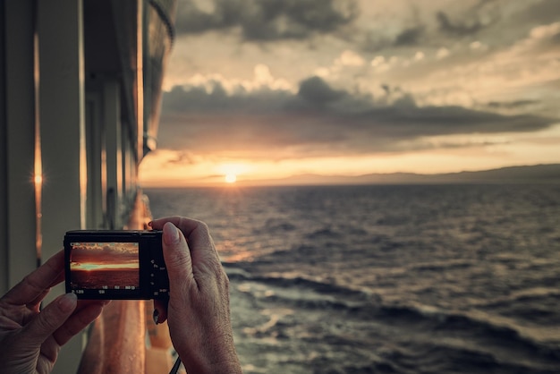 Foto mão cortada fotografando o mar de um barco durante o pôr-do-sol