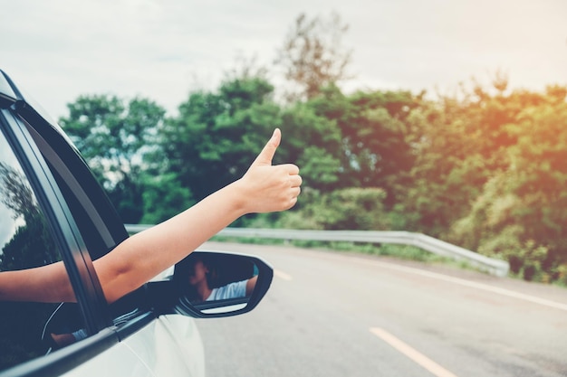 Mão cortada mostrando o dedo polegar para cima enquanto dirige o carro na estrada