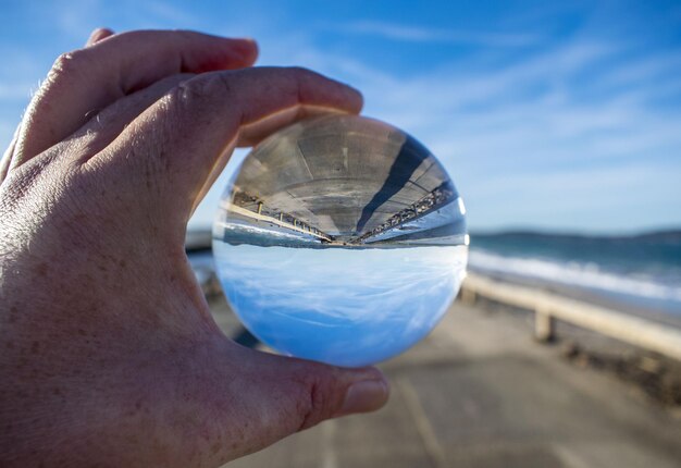 Mão cortada segurando bola de cristal com reflexo do mar e do cais
