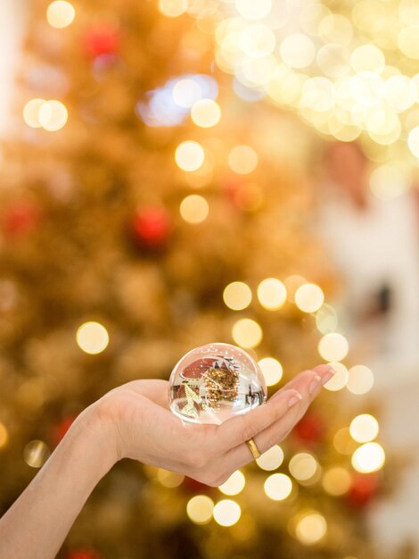 Foto mão cortada segurando bola de cristal contra a árvore de natal iluminada