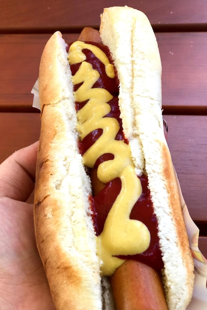 Foto mão cortada segurando cachorro-quente na mesa