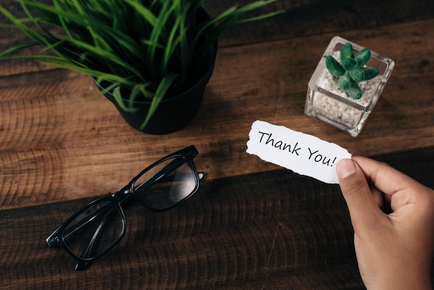 Mão cortada segurando cartão de agradecimento por plantas sobre a mesa