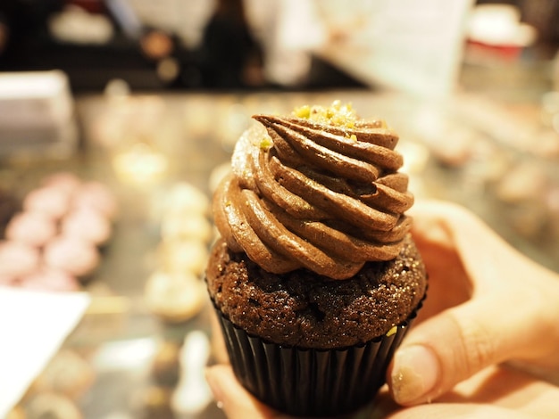 Foto mão cortada segurando cupcake adornado com creme de chocolate