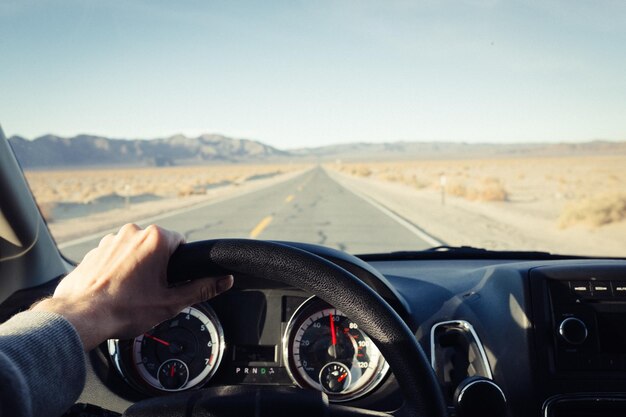 Foto mão cortada segurando o volante do carro contra o céu claro