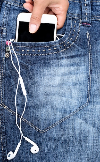 Mão cortada segurando telefone móvel em calças jeans.