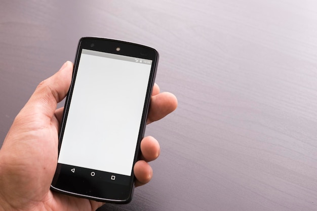 Mão cortada segurando um telefone celular sobre a mesa