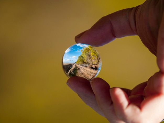 Foto mão cortada segurando uma bola de cristal com o reflexo de uma estrada de terra