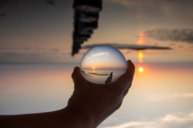 Foto mão cortada segurando uma bola de cristal com o reflexo do mar durante o pôr do sol