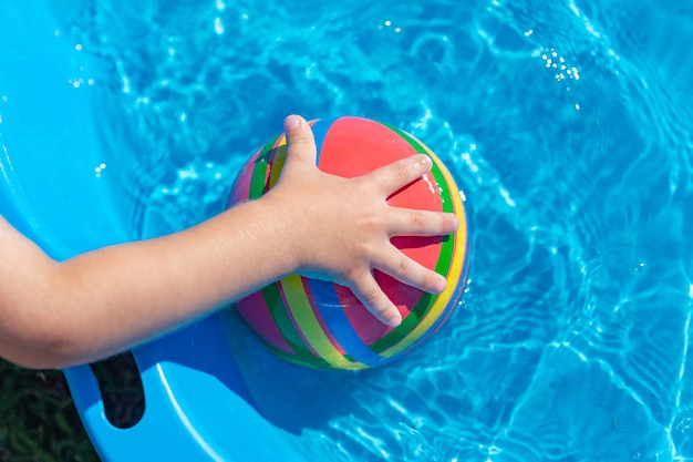 mão da criança segura uma bola na água em uma piscina rasa azul