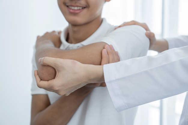 Foto mão da médica fazendo fisioterapia, estendendo o ombro de um paciente do sexo masculino.