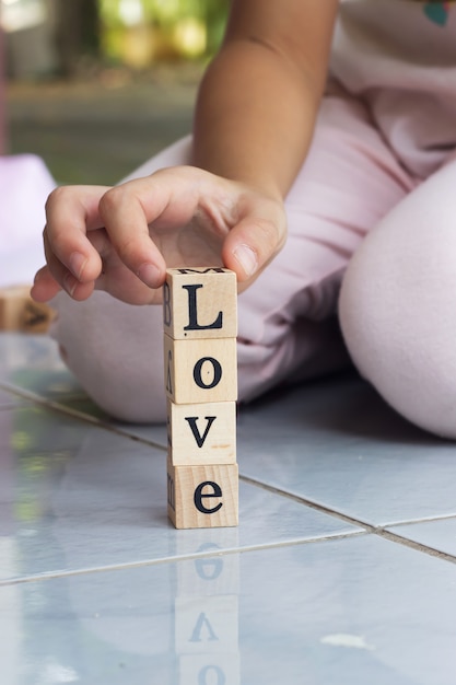 Foto mão da menina do close up que constrói o bloco de madeira na palavra do amor.