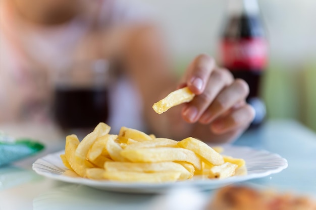 mão da menina pegando batatas fritas de um prato batatas fritas em um prato em luz brilhante em uma mesa colorida de perto