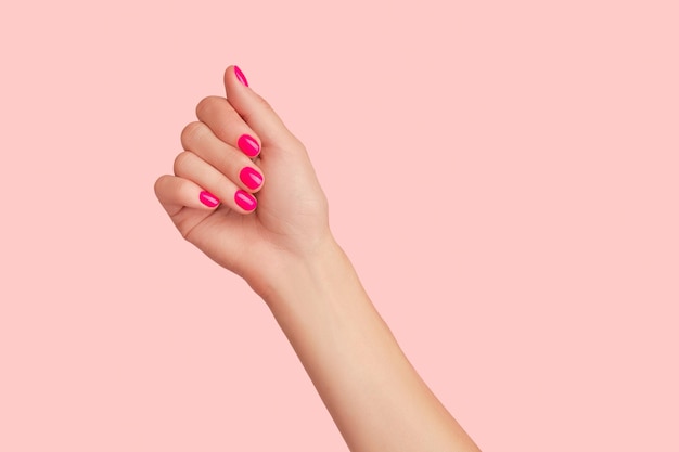 Mão da mulher com manicure na moda no conceito de salão de beleza de fundo rosa pastel