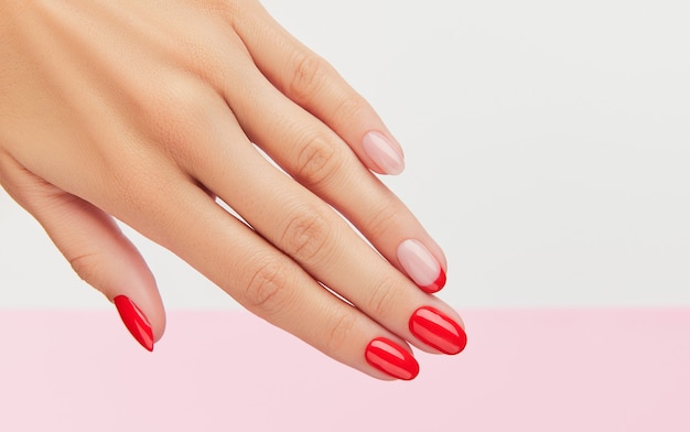 Mão da mulher com manicure vermelha na moda sobre fundo branco e rosa