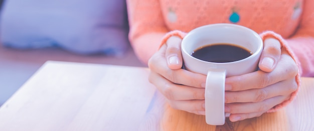 Mão da mulher na camiseta morna que guarda uma xícara de café para a bandeira da web.