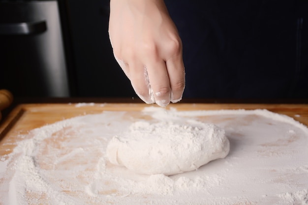 Mão da mulher que adiciona a farinha à massa de pão.