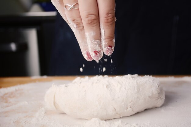 Mão da mulher que adiciona a farinha à massa de pão.