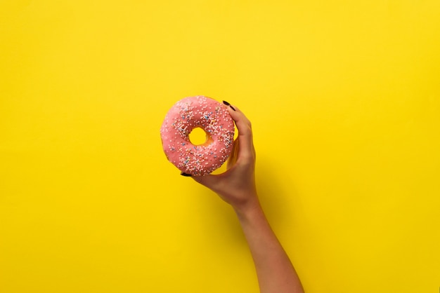 Mão da mulher que guarda a filhós cor-de-rosa deliciosa no fundo amarelo da cor.