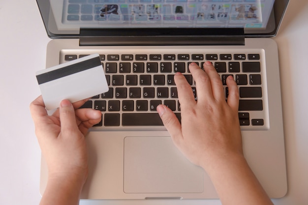 Mão da mulher que guarda o cartão de crédito e que usa o portátil que faz em linha. pagamento online, compras online
