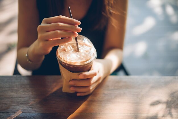 Mão da mulher que guarda o copo de café na tabela de madeira velha.