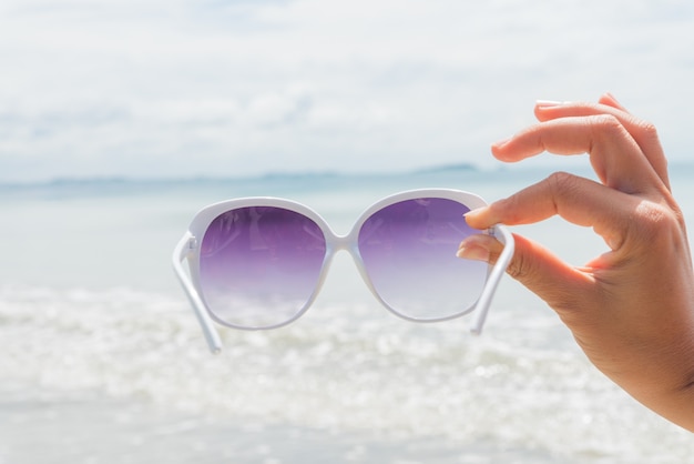 Mão da mulher que guarda óculos de sol sobre o mar para o conceito das férias de verão.