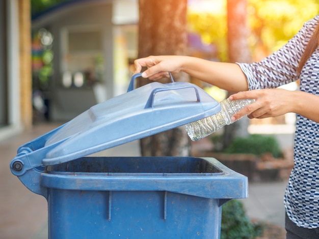 Mão da mulher que joga a garrafa de água plástica vazia no escaninho de reciclagem.