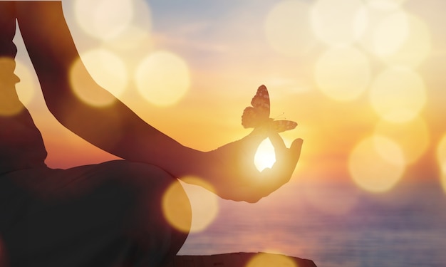 Mão da pessoa em uma pose de meditação e borboleta. Pôr do sol nas montanhas.