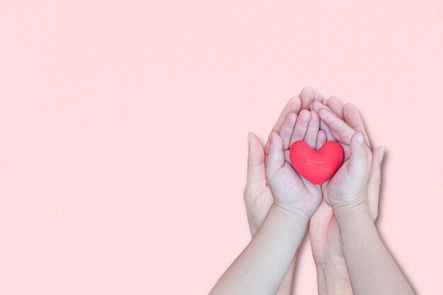mão de adulto e criança segurando coração vermelho em fundo rosa vista superior com cópia de espaço conceitos de dia dos namorados