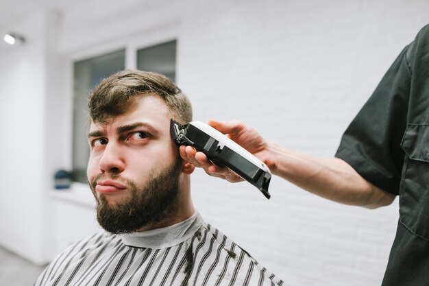 Mão de barbeiro com tosquiadeira corta cabelo de homem barbudo engraçado