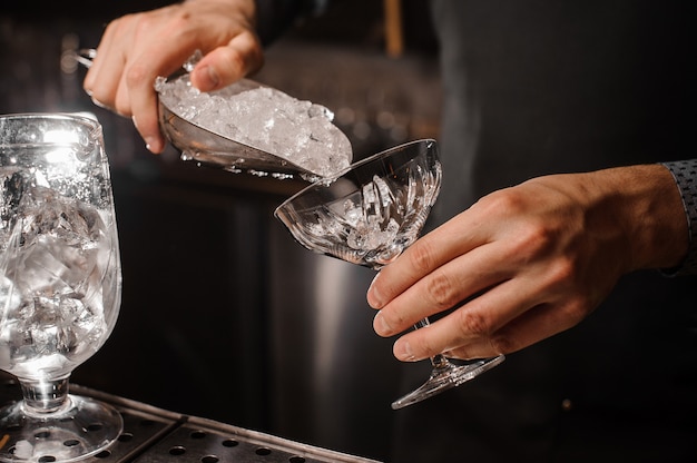 Mão de barman colocando gelo no copo de coquetel