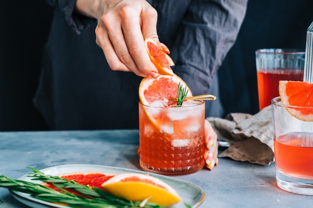 Mão de barman espreme suco de toranja fresca em coquetel de limonada com gelo e alecrim.